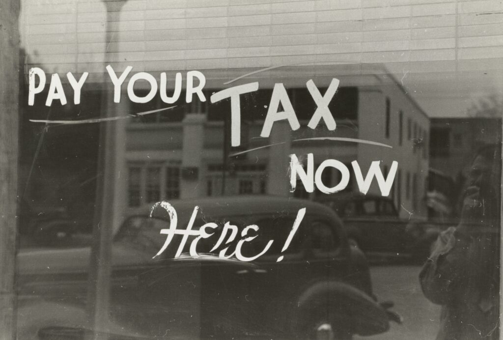 Old, 1930-1940 picture with words on storefront glass saying "Pay your tax here!"