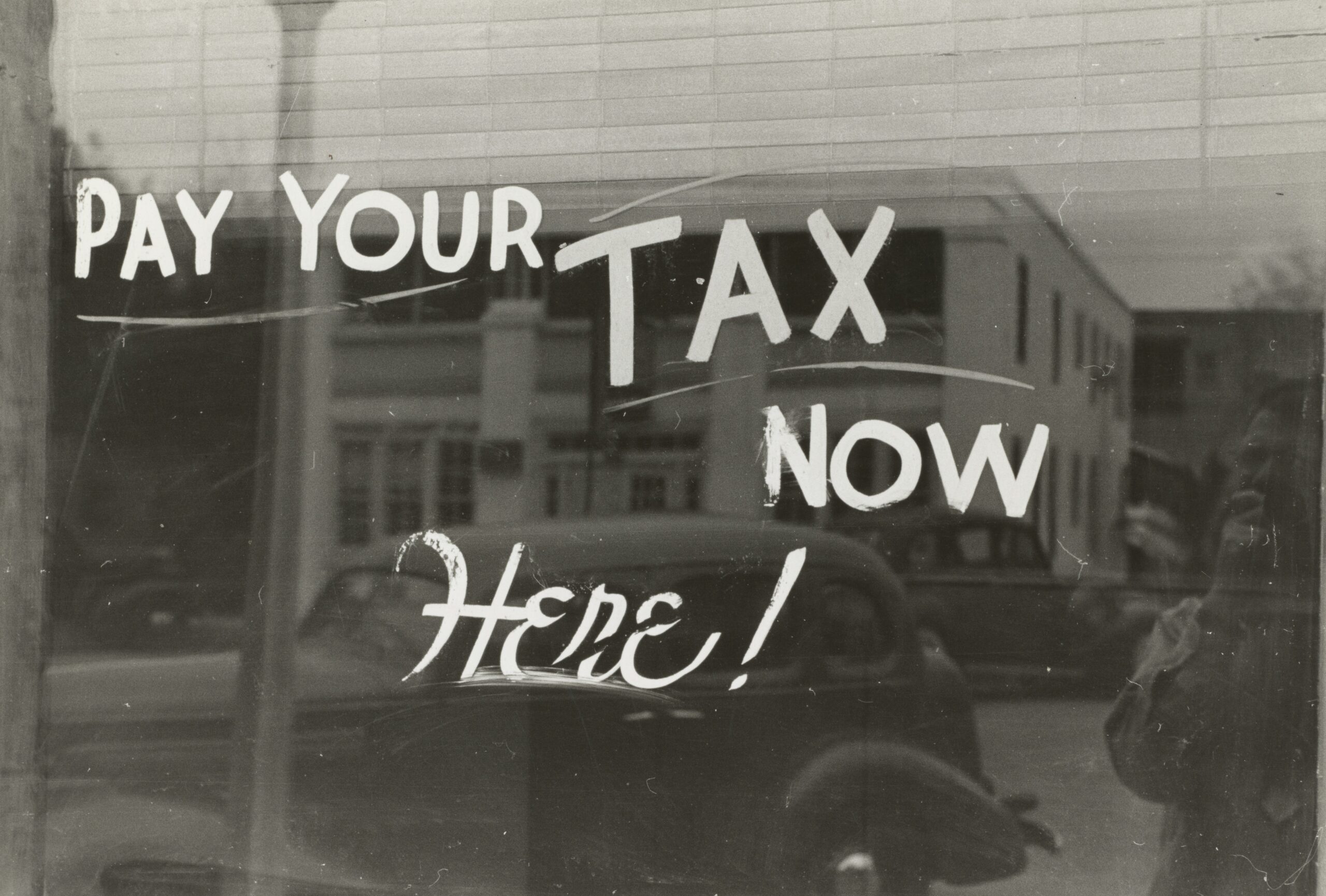 Old, 1930-1940 picture with words on storefront glass saying "Pay your tax here!"